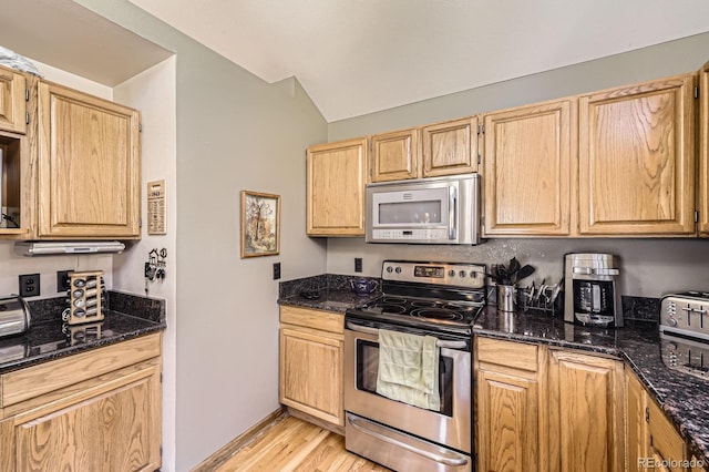 kitchen featuring dark stone countertops, light wood finished floors, lofted ceiling, and stainless steel appliances