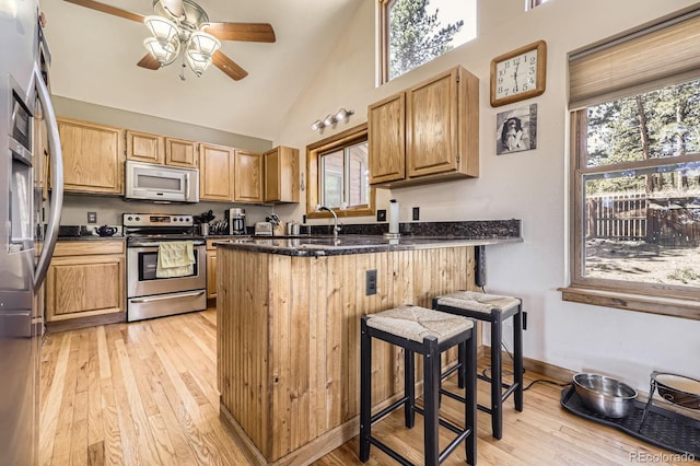 kitchen with light wood-type flooring, a ceiling fan, a peninsula, white microwave, and stainless steel electric range