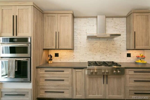 9768 Otis Dr, Westminster, CO 80021 - kitchen featuring light brown cabinets, dark countertops, wall chimney exhaust hood, backsplash, and stainless steel appliances