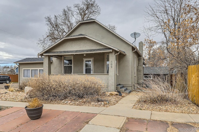 bungalow featuring fence, a chimney, and stucco siding