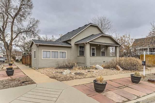 bungalow-style house with roof with shingles, fence, and stucco siding