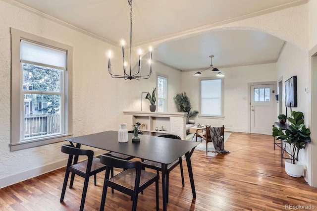 dining space with crown molding, arched walkways, wood-type flooring, and a textured wall