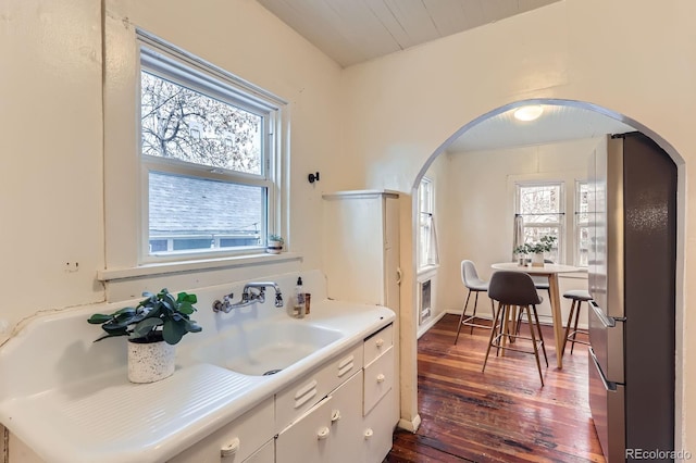 kitchen with arched walkways, dark wood finished floors, light countertops, freestanding refrigerator, and a sink