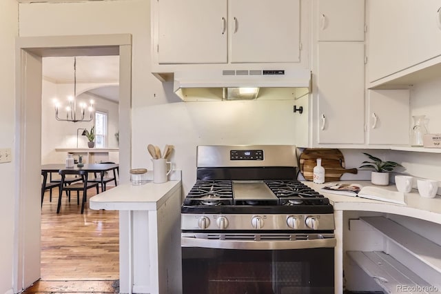 kitchen with stainless steel gas stove, white cabinets, light countertops, under cabinet range hood, and a chandelier