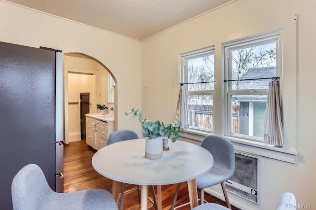 dining space with arched walkways and dark wood-type flooring