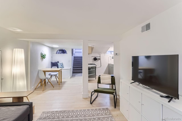 living room featuring stairway, light wood-type flooring, and visible vents