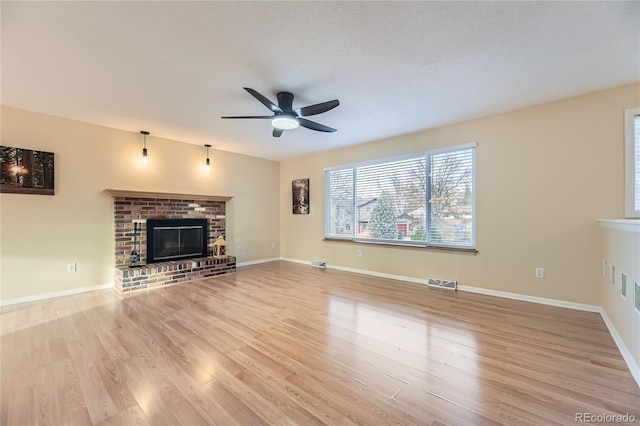 unfurnished living room with ceiling fan, a fireplace, light hardwood / wood-style floors, and a textured ceiling