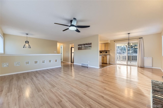 unfurnished living room featuring ceiling fan with notable chandelier and light wood-type flooring