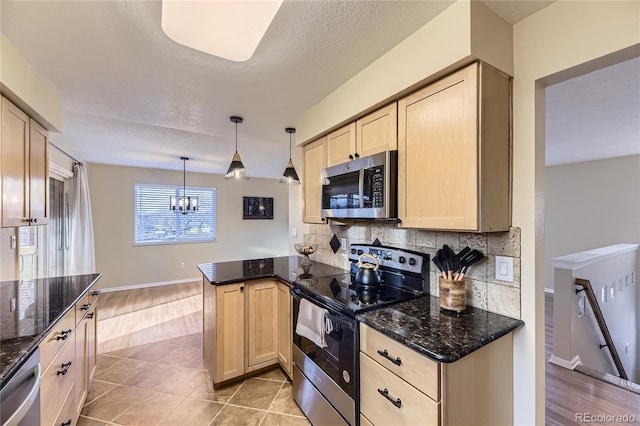 kitchen with light brown cabinets, backsplash, appliances with stainless steel finishes, decorative light fixtures, and kitchen peninsula