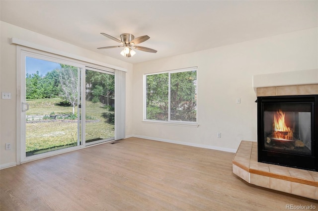 unfurnished living room with ceiling fan, a fireplace, and light wood-type flooring