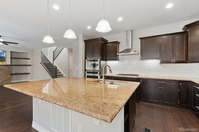 kitchen featuring a kitchen island with sink, stainless steel appliances, wall chimney exhaust hood, sink, and backsplash