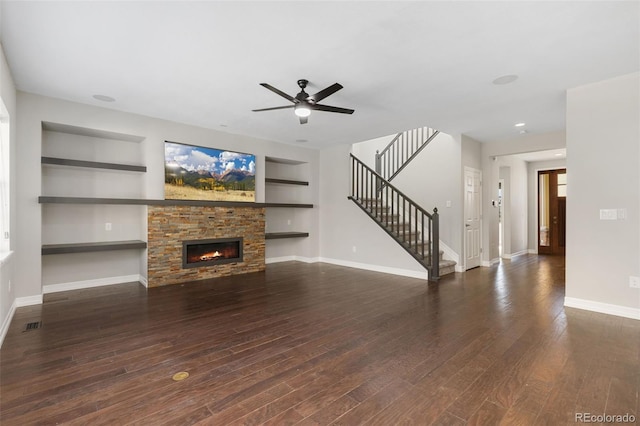 unfurnished living room with built in shelves, dark wood-type flooring, ceiling fan, and a fireplace