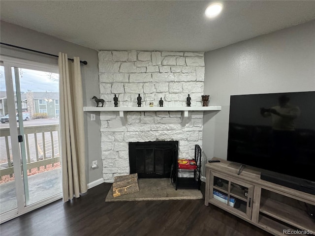 living room with dark hardwood / wood-style floors, a stone fireplace, and a textured ceiling