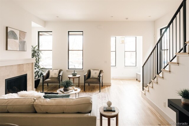 living room with baseboards, a fireplace, light wood-style floors, and stairs