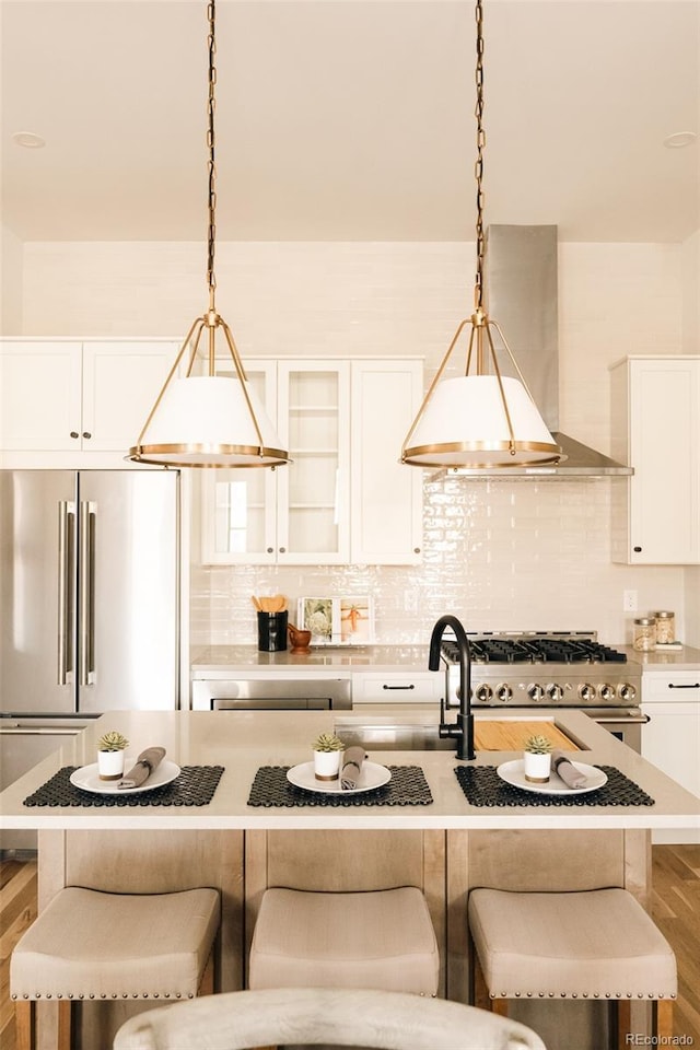 kitchen with high end appliances, a breakfast bar area, backsplash, and wall chimney exhaust hood