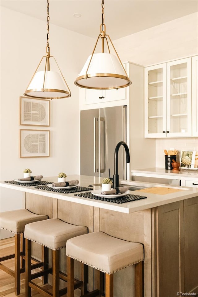 kitchen with light countertops, high end fridge, a kitchen bar, hanging light fixtures, and glass insert cabinets