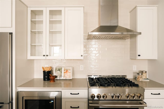 kitchen with wall chimney range hood, white cabinets, stainless steel appliances, and decorative backsplash