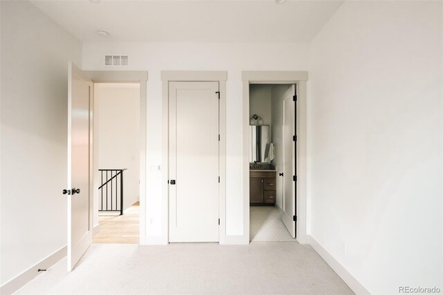 unfurnished bedroom featuring baseboards, ensuite bathroom, visible vents, and light carpet
