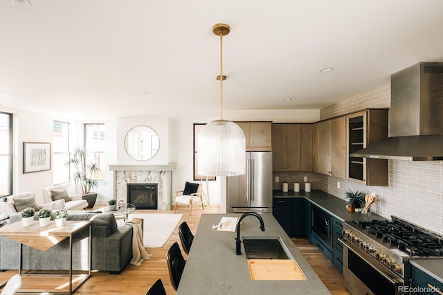 kitchen with a high end fireplace, wall chimney range hood, backsplash, a sink, and high end appliances