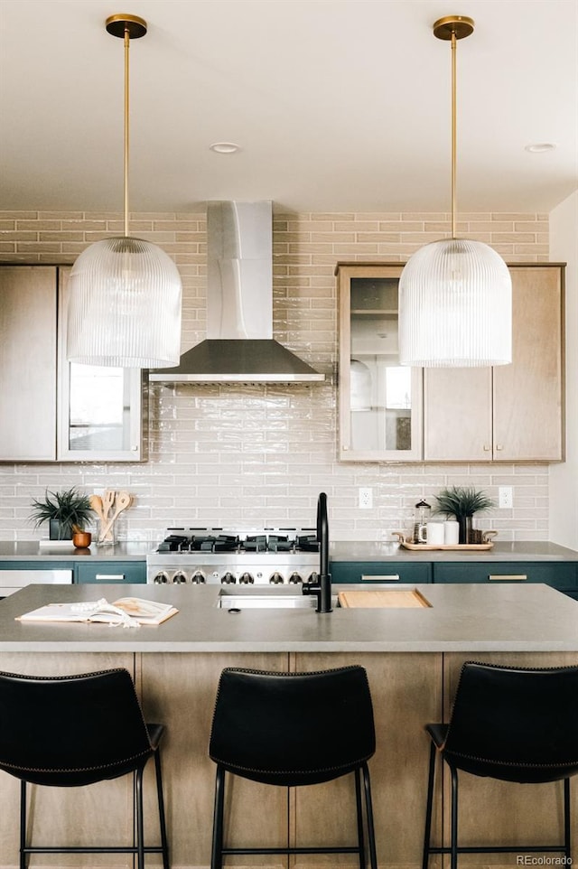 kitchen with wall chimney range hood, tasteful backsplash, decorative light fixtures, and a breakfast bar