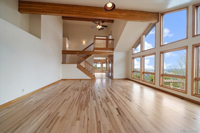 23007 Big Game Trl, Conifer, CO 80433 - unfurnished living room featuring high vaulted ceiling, beamed ceiling, stairs, light wood-style flooring, and a ceiling fan