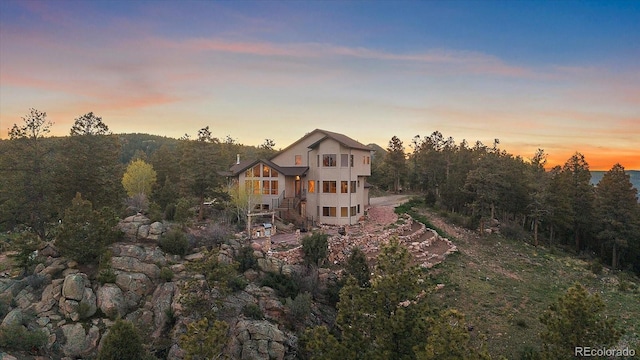 23007 Big Game Trl, Conifer, CO 80433 - back of house at dusk with stairway, a balcony, a wooded view, and stucco siding