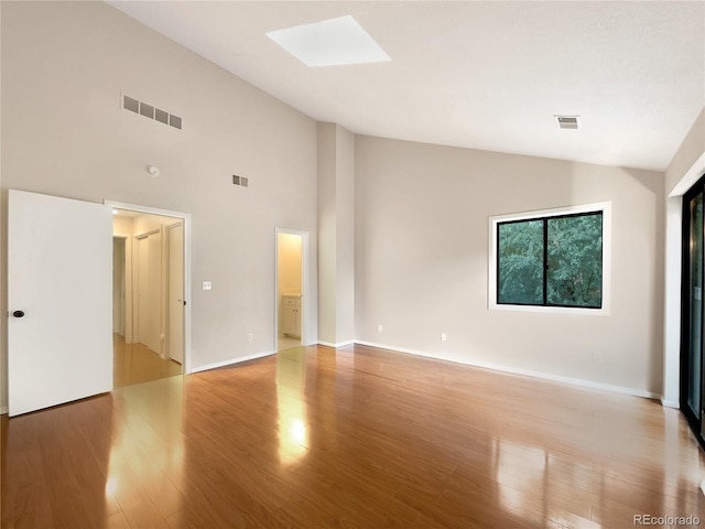 unfurnished room featuring light wood-type flooring, a skylight, and high vaulted ceiling