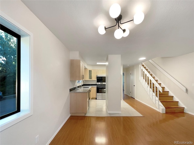 kitchen featuring light brown cabinetry, light wood-type flooring, stainless steel range, sink, and a chandelier