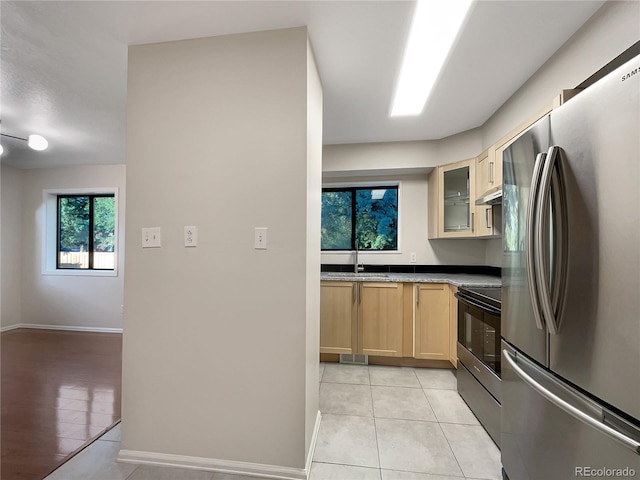 kitchen featuring stainless steel refrigerator, sink, black / electric stove, light brown cabinetry, and light tile patterned flooring