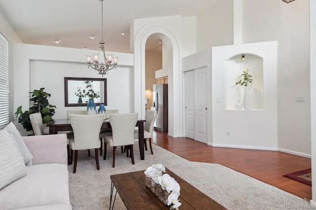 dining space featuring an inviting chandelier, a high ceiling, arched walkways, and wood finished floors