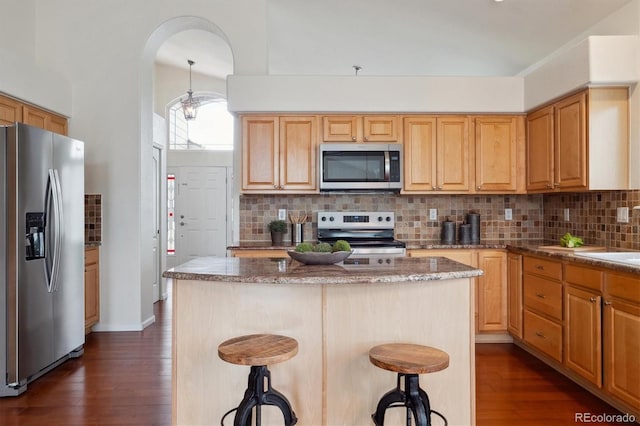 kitchen featuring appliances with stainless steel finishes, a breakfast bar, decorative backsplash, and dark wood-style floors