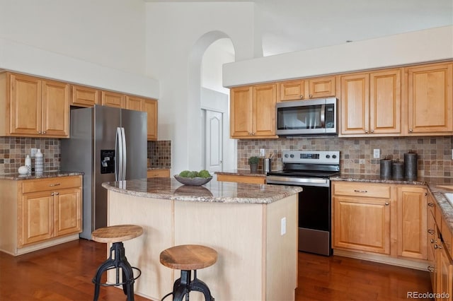 kitchen featuring stone countertops, dark wood-style flooring, a center island, stainless steel appliances, and a kitchen bar