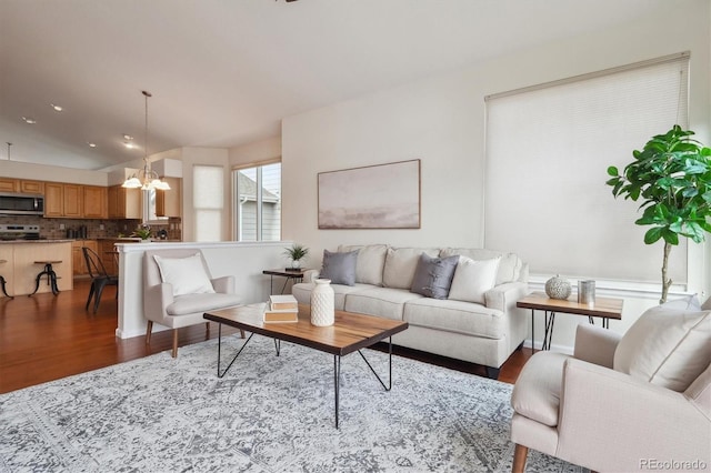 living area with an inviting chandelier, vaulted ceiling, and wood finished floors