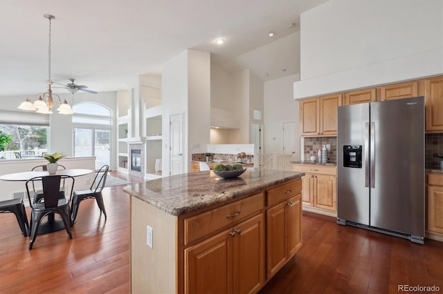 kitchen with stainless steel fridge, stone countertops, a glass covered fireplace, dark wood-style floors, and high vaulted ceiling