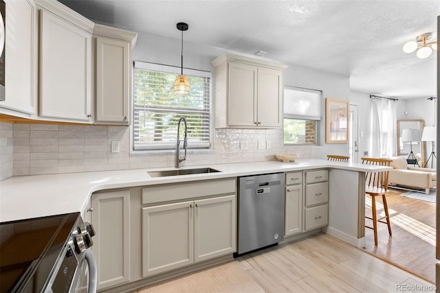 kitchen with a kitchen bar, sink, hanging light fixtures, appliances with stainless steel finishes, and light hardwood / wood-style floors