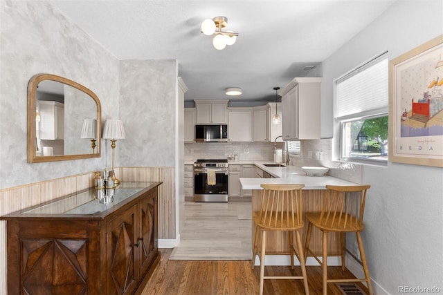 kitchen with a breakfast bar, sink, white cabinets, stainless steel appliances, and light hardwood / wood-style flooring