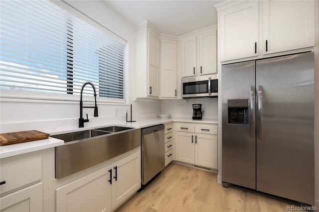 kitchen with stainless steel appliances, light countertops, light wood-style floors, white cabinetry, and a sink