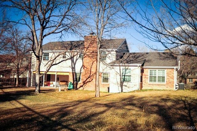 back of property featuring a yard, fence, brick siding, and a chimney