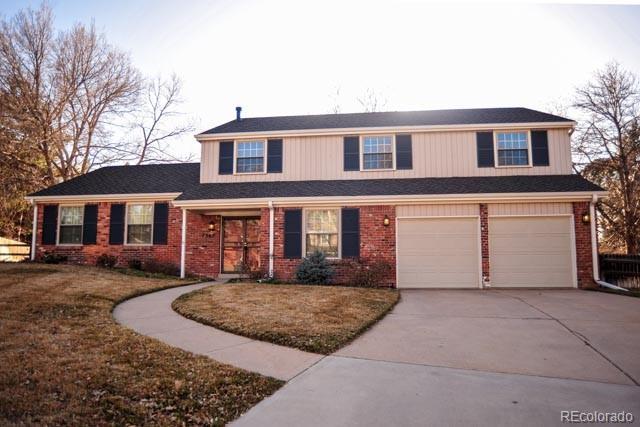 traditional home with concrete driveway, an attached garage, brick siding, and a front lawn