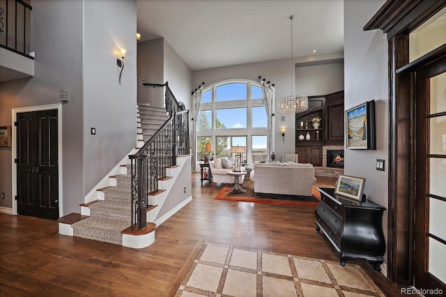 foyer with wood finished floors, stairway, a chandelier, a fireplace, and a high ceiling