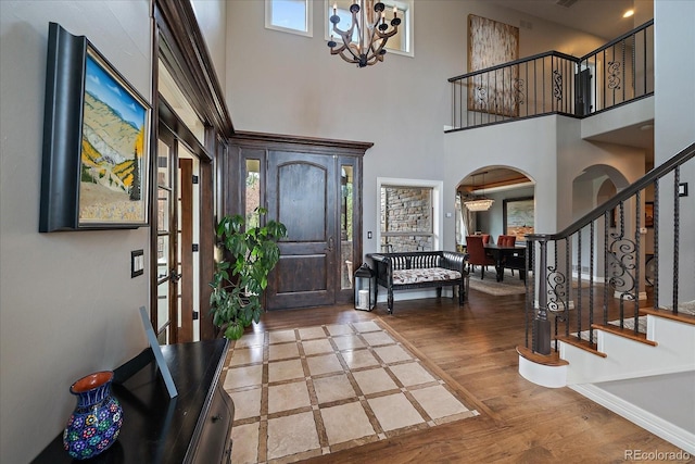 entryway featuring stairs, wood finished floors, arched walkways, a high ceiling, and a notable chandelier
