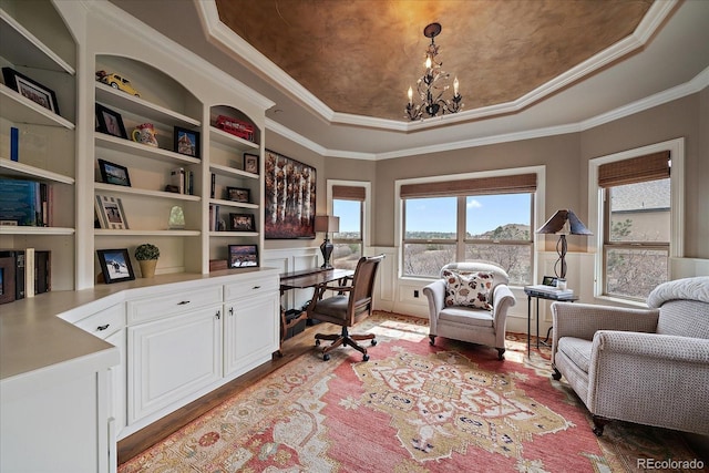 home office featuring a tray ceiling, a chandelier, crown molding, built in desk, and light wood-type flooring