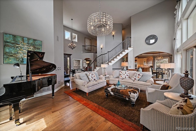 living room with an inviting chandelier, hardwood / wood-style floors, stairway, a towering ceiling, and arched walkways