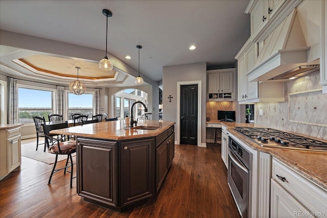 kitchen with a breakfast bar area, a sink, appliances with stainless steel finishes, tasteful backsplash, and custom exhaust hood