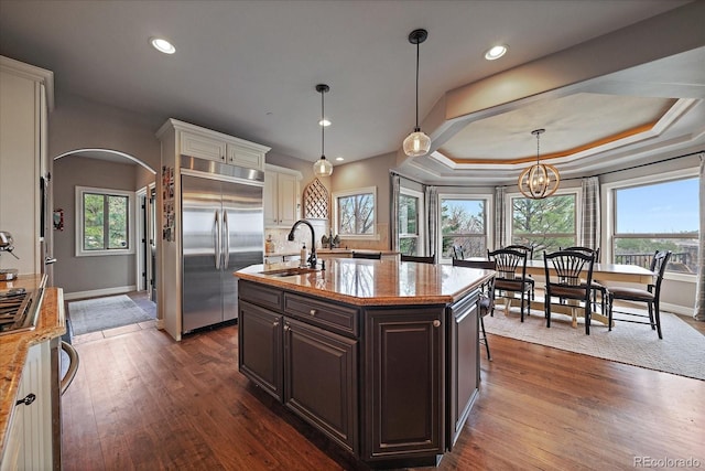 kitchen featuring dark brown cabinets, stainless steel built in fridge, a sink, dark wood-type flooring, and arched walkways
