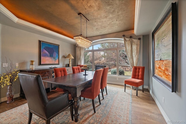 dining area featuring a raised ceiling, baseboards, a notable chandelier, and light wood-style floors