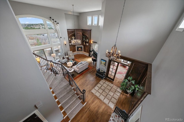 staircase featuring a lit fireplace, a chandelier, a towering ceiling, and wood finished floors