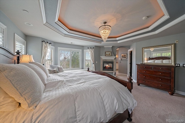 carpeted bedroom featuring an inviting chandelier, arched walkways, a tray ceiling, baseboards, and a multi sided fireplace