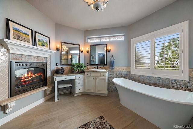 bathroom featuring a tile fireplace, tile walls, vanity, and a freestanding tub
