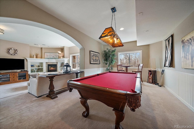 recreation room featuring a wainscoted wall, light colored carpet, pool table, a fireplace, and arched walkways
